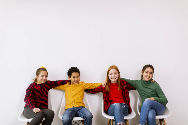 Retrato de lindos niños pequeños en jeans sentados en sillas contra la pared blanca - Foto, imagen