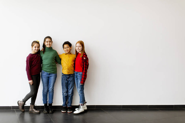 Portrait of cute little kids in jeans  looking at camera and smiling, standing against the white wall - Foto, Imagem