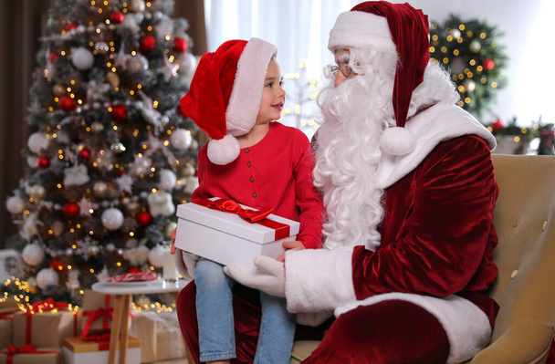 Kerstman geeft cadeautje aan klein meisje in kamer versierd voor Kerstmis - Foto, afbeelding