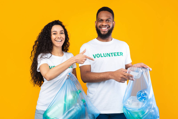 Wielokulturowi wolontariusze zbierający plastik w workach na śmieci na żółtym tle - Zdjęcie, obraz