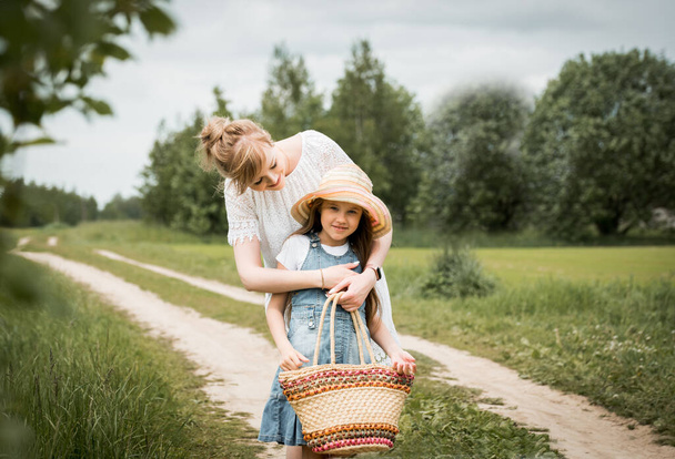 mother and daughter walking in the forest and holding hands.walk along the path. field and nature. Wicker basket. maternal love, happy childhood.mom hugs a girl, care and education, family concept. - Foto, immagini