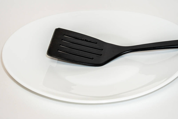 Black plastic kitchen spatula on white plate - Photo, Image