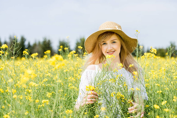 Portrait of a happy cute girl in a summer wheat field, in a white dress and hat.yellow rapeseed flowers. sunny summer day outdoors - Fotografie, Obrázek