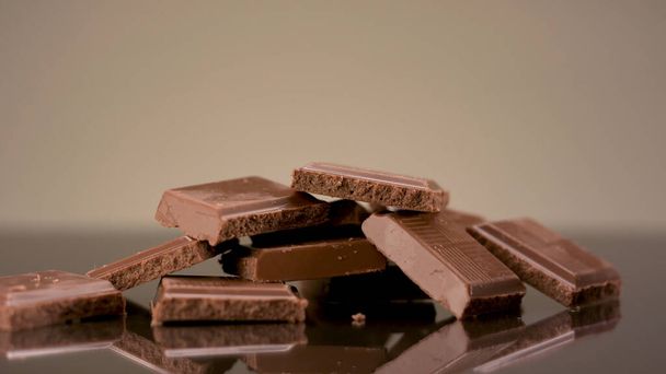 Großaufnahme von Milch leckeren Schokoladenstücken, die auf dem Tisch liegen. Archivmaterial. Zerbrochene Schokoriegel isoliert auf beigem Hintergrund, Konzept von Süßigkeiten und Süßwaren.  - Foto, Bild