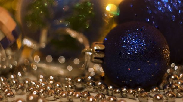 Großaufnahme einer Mädchenhand, die eine blau leuchtende Weihnachtskugel aus Plastik in die Nähe silberner kleiner Perlen legt. Konzept. Neujahrsferien, Spielzeug und blinkende Girlanden für die Fichtendekoration. - Foto, Bild