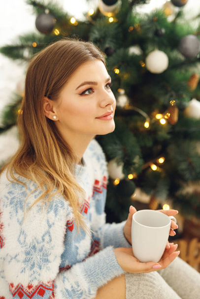 Close up of girl wears festive clothes take cup of coffee at home near Christmas Tree - Foto, Imagen