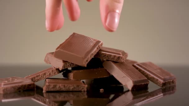 Close-up van de hand nemen van een stuk melk smakelijke chocolade liggend op de tafel. Voorraadbeelden. Gebroken chocoladereep geïsoleerd op beige achtergrond, concept van snoep en snoep. - Video