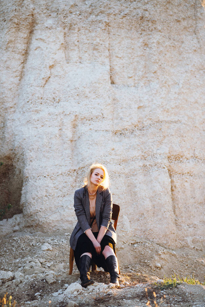 Chica pelirroja sentada en una silla vieja en un cañón de arena al atardecer. Retrato psicológico de la soledad. Hipster viejo concepto de moda - Foto, Imagen
