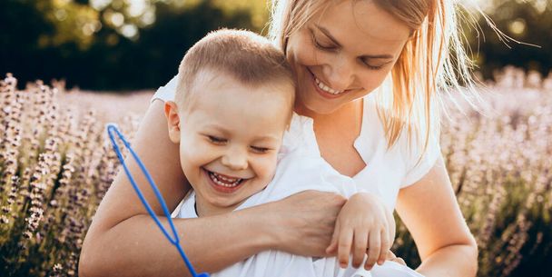 Okouzlující matka a její syn se usmívá a objímají v levandulovém poli dělat balónky se speciální hračkou - Fotografie, Obrázek