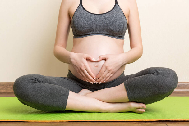 Beautiful pregnant woman doing yoga at home. Pregnancy Yoga and Fitness concept at coronavirus time. - 写真・画像