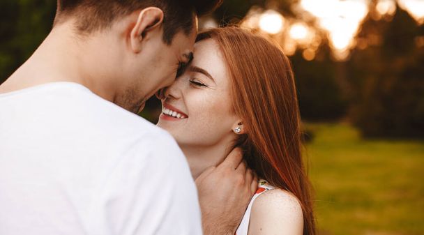 Back view photo of a caucasian lady with freckles and red hair and her husband kissing and embracing the park - Photo, Image