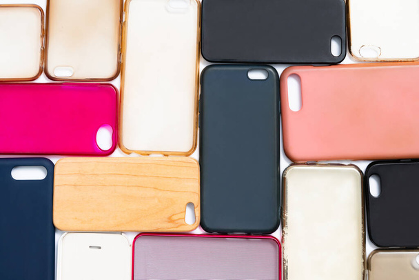 Stapel veelkleurige plastic achterhoezen voor mobiele telefoon. Keuze uit accessoires voor smartphonebeschermers op een witte achtergrond. Veel siliconen telefoon ruggen of huiden naast elkaar - Foto, afbeelding
