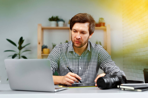 Young man photographer sits at table and works from home - Foto, imagen