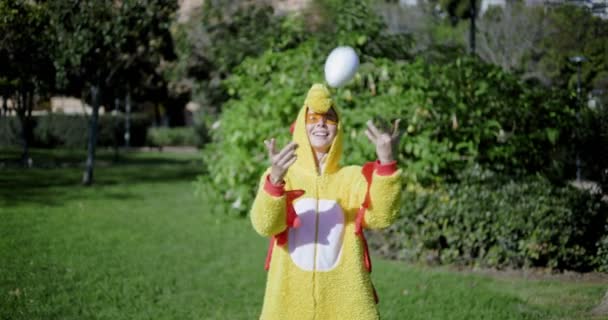 Ένα κορίτσι ντυμένο σαν κοτόπουλο πετάει ένα αυγό από πάνω και το πιάνει πίσω. Αστείο βίντεο με μια γυναίκα με στολή κοτόπουλου. Κοτόπουλο με αυγό. Το κορίτσι και το αυγό κοτόπουλου.. - Πλάνα, βίντεο