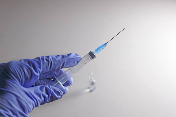 Hand in medical glove holds syringe with covid 19 antidote over avial standing on table. Selective focus - Foto, immagini