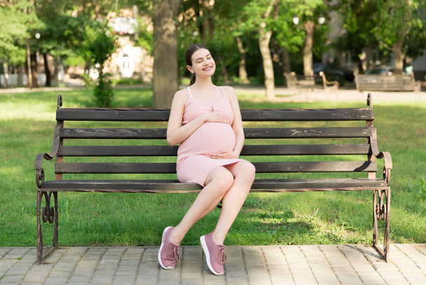 Schwangere junge Frau auf Bank im Park. Schwangerschaft und Mutterschaft. Gesunder Lebensstil. - Foto, Bild