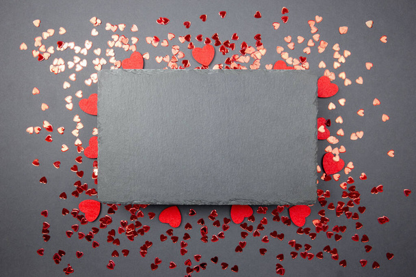 Carte de voeux Saint-Valentin avec confettis cœurs rouges et tableau noir en ardoise sur fond sombre. Vue de dessus avec espace pour vos salutations. Couché à plat, maquette. - Photo, image