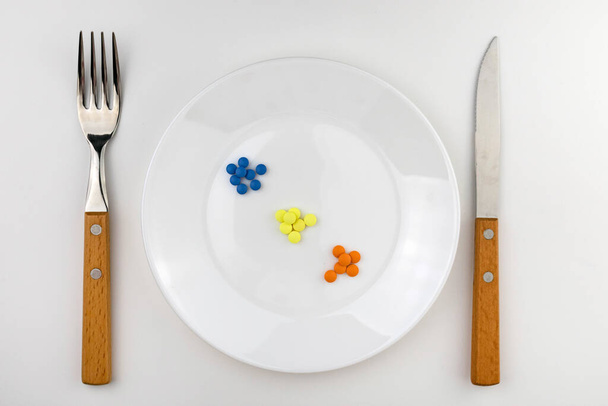 Table setting with a white plate filled with various capsules next to the cutlery on a white background. - Foto, afbeelding
