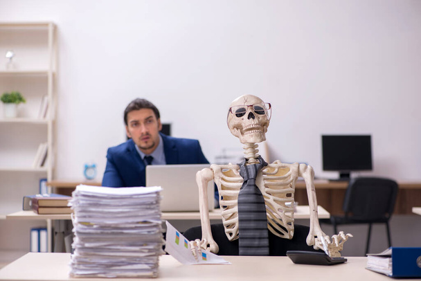 Joven empleado masculino con esqueletos en la oficina - Foto, imagen