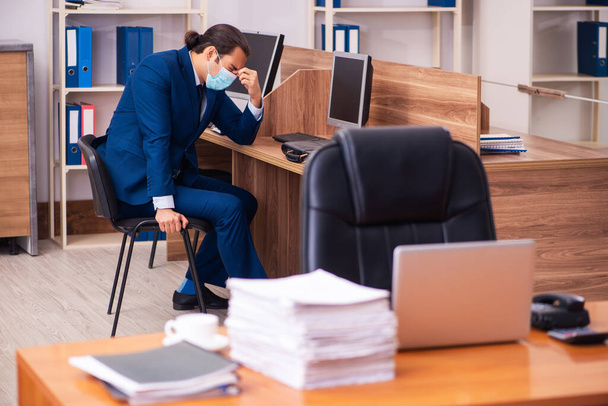 Молодий працівник чоловічої статі працює в офісі в масці
 - Фото, зображення