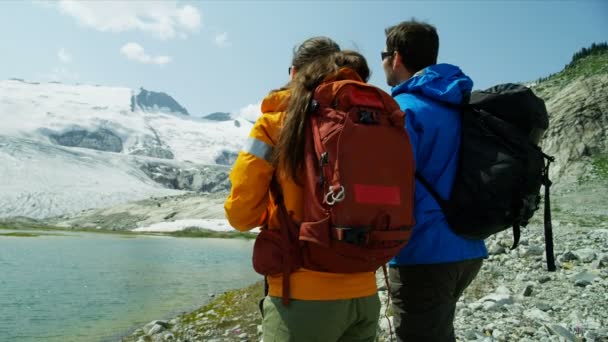 Coppia caucasica che osserva il lago glaciale panoramico all'aperto e il ghiacciaio in estate rilassarsi nella natura selvaggia di montagna  - Filmati, video