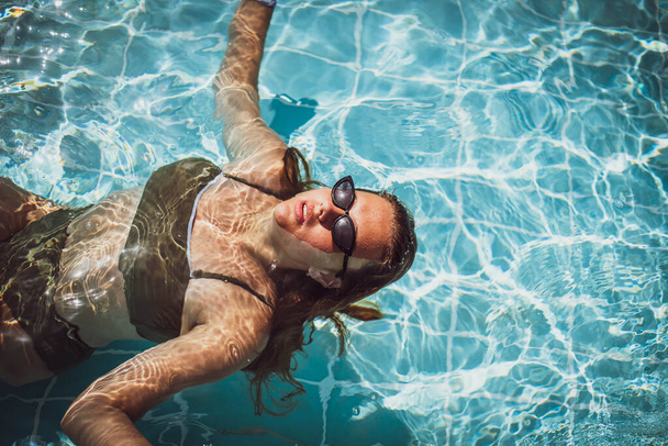 Portrait de mode de fille mignonne gracieuse dans des lunettes de soleil élégantes posant dans la piscine pendant les vacances sur la station de luxe. Joyeux plus la taille de l'adolescente profiter. heureux, émotion positive, style d'été. - Photo, image