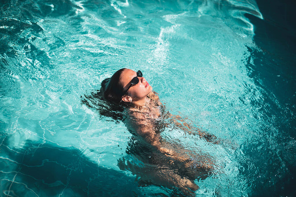 Retrato de moda de la elegante chica linda en gafas de sol elegantes posando en la piscina durante las vacaciones en el complejo de lujo. Alegre más tamaño adolescente disfrutando. feliz, emoción positiva, estilo de verano. - Foto, imagen
