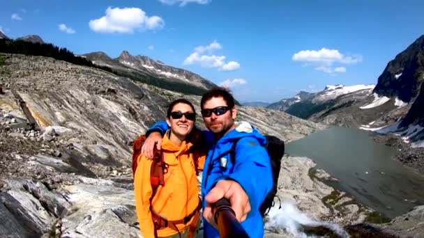 Πορτρέτο άποψη του ευτυχισμένου ζευγαριού Heli πεζοπορία λήψη selfie ψηλά στα βουνά κοντά στο ποτάμι και παγετώνα λίμνη Βρετανική Κολομβία Καναδά   - Πλάνα, βίντεο