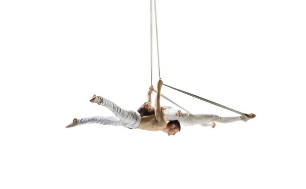 Couple of young acrobats, circus athletes isolated on white studio background. Training perfect balanced in flight - Φωτογραφία, εικόνα
