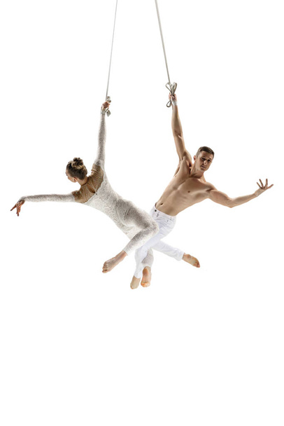 Couple of young acrobats, circus athletes isolated on white studio background. Training perfect balanced in flight - Фото, изображение