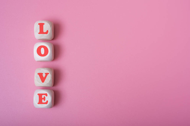 La palabra amor tiene la forma de un corazón sobre cubos de madera sobre un fondo rosa. Amor, romance, relación o concepto de San Valentín. - Foto, imagen