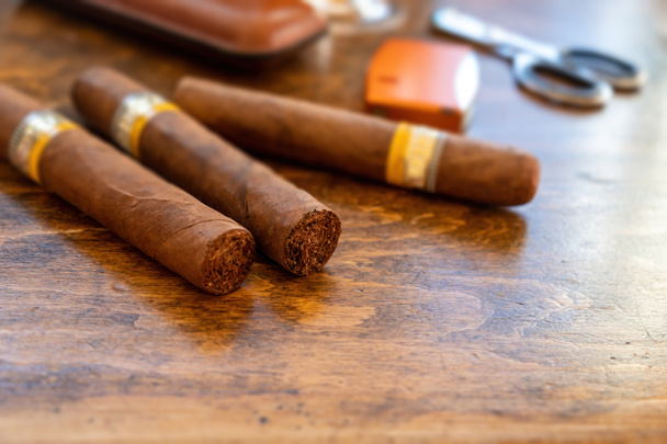Cygara i akcesoria na drewnianym biurku, widok z bliska. Kubański jakości tytoń do cygar palenia luksusowy styl życia. - Zdjęcie, obraz