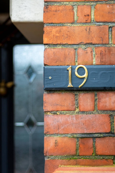 Auf einer blauen Plakette an einer roten Ziegelwand steht die Hausnummer 19. - Foto, Bild