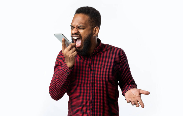 Θυμωμένος μαύρος τύπος φωνάζει στο Smartphone στέκεται πάνω από το λευκό φόντο - Φωτογραφία, εικόνα