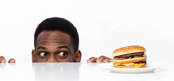 Nälkäinen afrikkalainen kaveri katselee Burger pöydällä studiossa - Valokuva, kuva