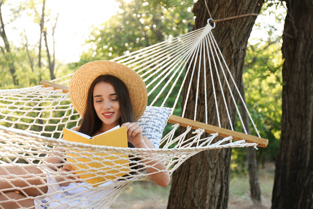 Young woman reading book in comfortable hammock at green garden - Zdjęcie, obraz