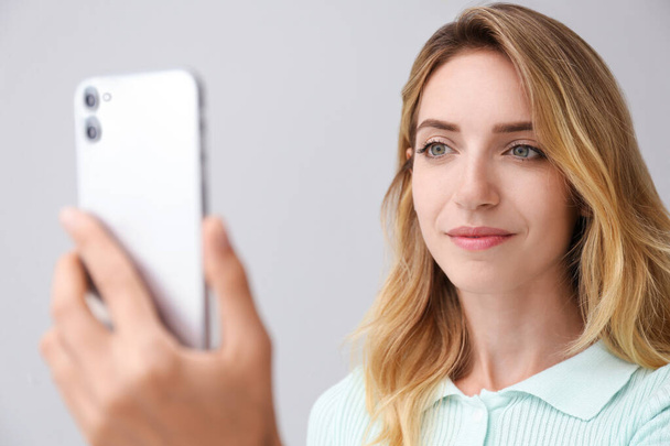 Gri arka planda yüz tarayıcısı olan akıllı telefonun kilidini açan genç bir kadın. Biyometrik doğrulama - Fotoğraf, Görsel