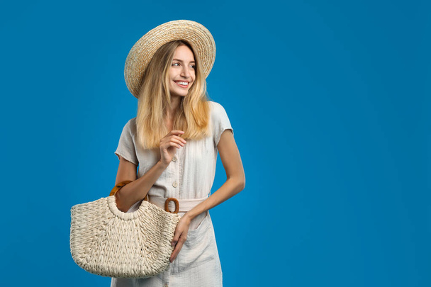 Beautiful young woman with stylish straw bag on blue background. Space for text - Foto, immagini