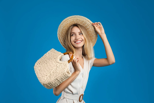 Beautiful young woman with stylish straw bag on blue background - Foto, immagini