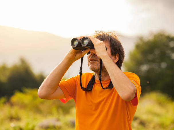 The hiker does bird watching with binoculars in the mountain nature park in search of birds of prey. Man scans the sky with binoculars. Concept of person looking to the future. - Foto, Bild