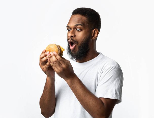 eccitati nero uomo holding hamburger in piedi su bianco studio sfondo - Foto, immagini