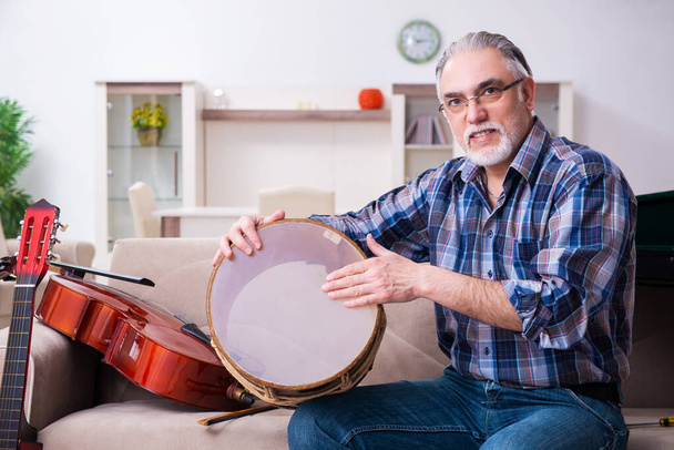 Hombre mayor reparador reparando instrumentos musicales en casa - Foto, imagen