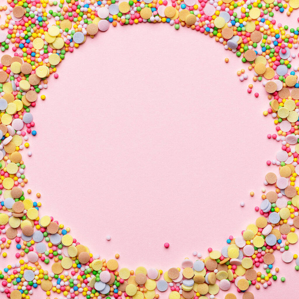 Süßes Kuchengebäck Zutat. Zuckerstreusel in Kreisform. Rundrahmen mit Teigbelag. Leere Gestaltung in der Mitte. Vereinzelt auf rosa Hintergrund. Ferien- und Geburtstagskonzept - Foto, Bild