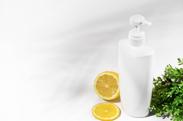 Λευκό μη επώνυμα μπουκάλι με λεμόνι και πράσινα φυτά. Δοχείο με διανομέα φυσικά καλλυντικά προϊόντα. Κενό διάκοσμο για λοσιόν, κρέμα, λοσιόν σώματος, σαμπουάν ή μαλακτικό μαλλιών. Στυλ Mockup - Φωτογραφία, εικόνα