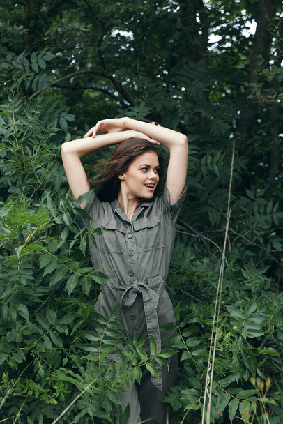 mujer en el bosque sostiene sus manos detrás de su cabeza y mira hacia otro lado así la naturaleza viaja  - Foto, imagen