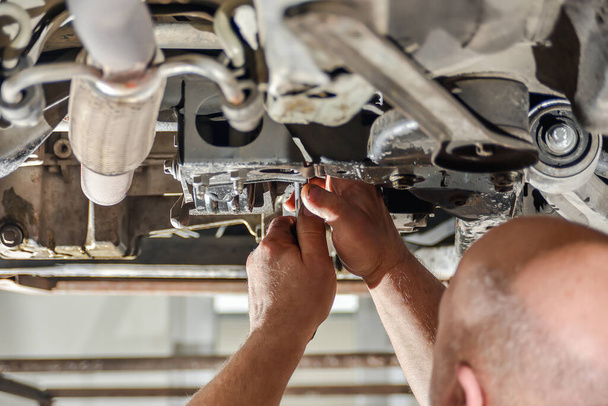 Ein Automechaniker repariert das Fahrgestell eines Autos, das auf einer Hebebühne steht. - Foto, Bild