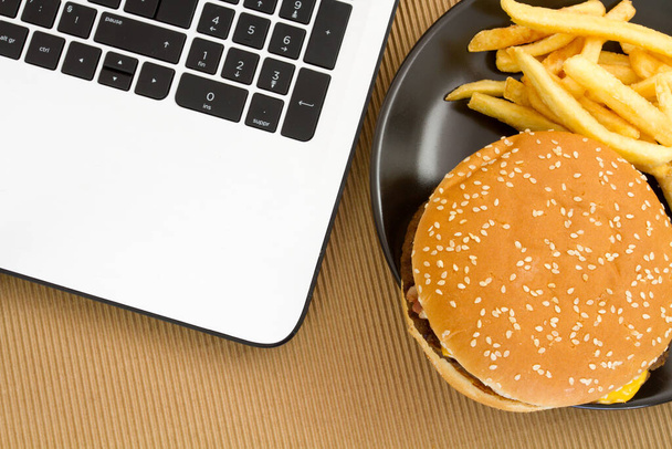 cheeseburger and French fries on plate near laptop - Photo, image