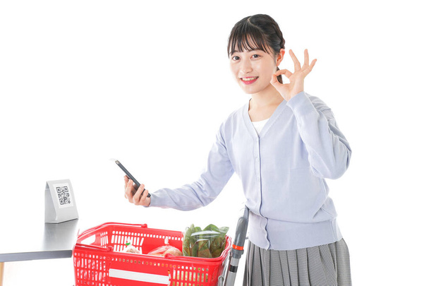 woman with full trolley basket scanning QR code by her phone - Photo, Image