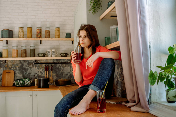 Healthy food. Breakfast of freshly squeezed fruit. pretty woman holding glass with tasty red cherry or strawberry juice. In the kitchen sitting on the table. Exotic Indoor Plants.Modern lifestyle - Foto, imagen