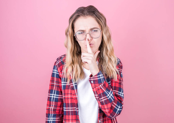 Young girl on a pink background asking for silence with a finger on her lips. Silence and secret concept. - Foto, Imagen